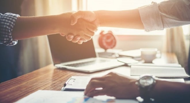 hand shake over a wooden table with a laptop in the background